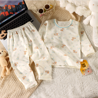 Children's pajama set with teddy bear pattern on a textured surface with a laptop and coffee.