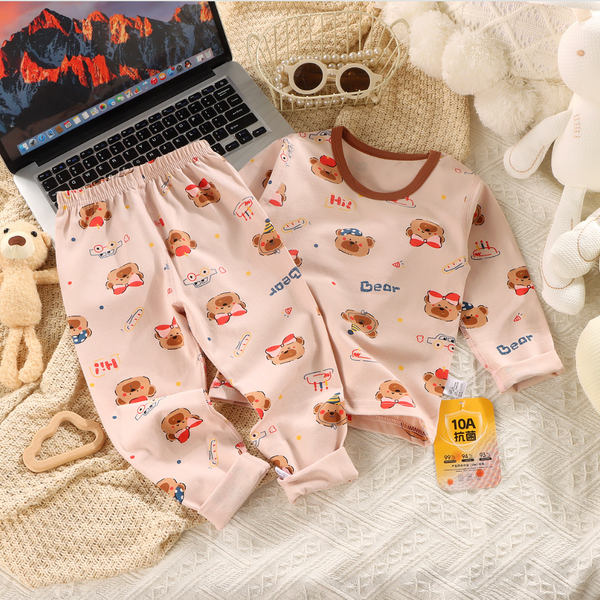 Children's pajama set with bear pattern on a textured surface with a laptop and bottle.