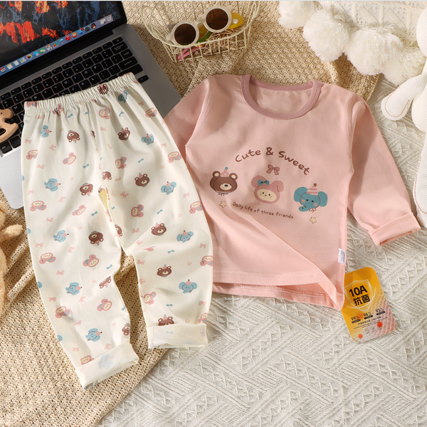 Children's pink shirt and white pants with bear designs on a textured surface.