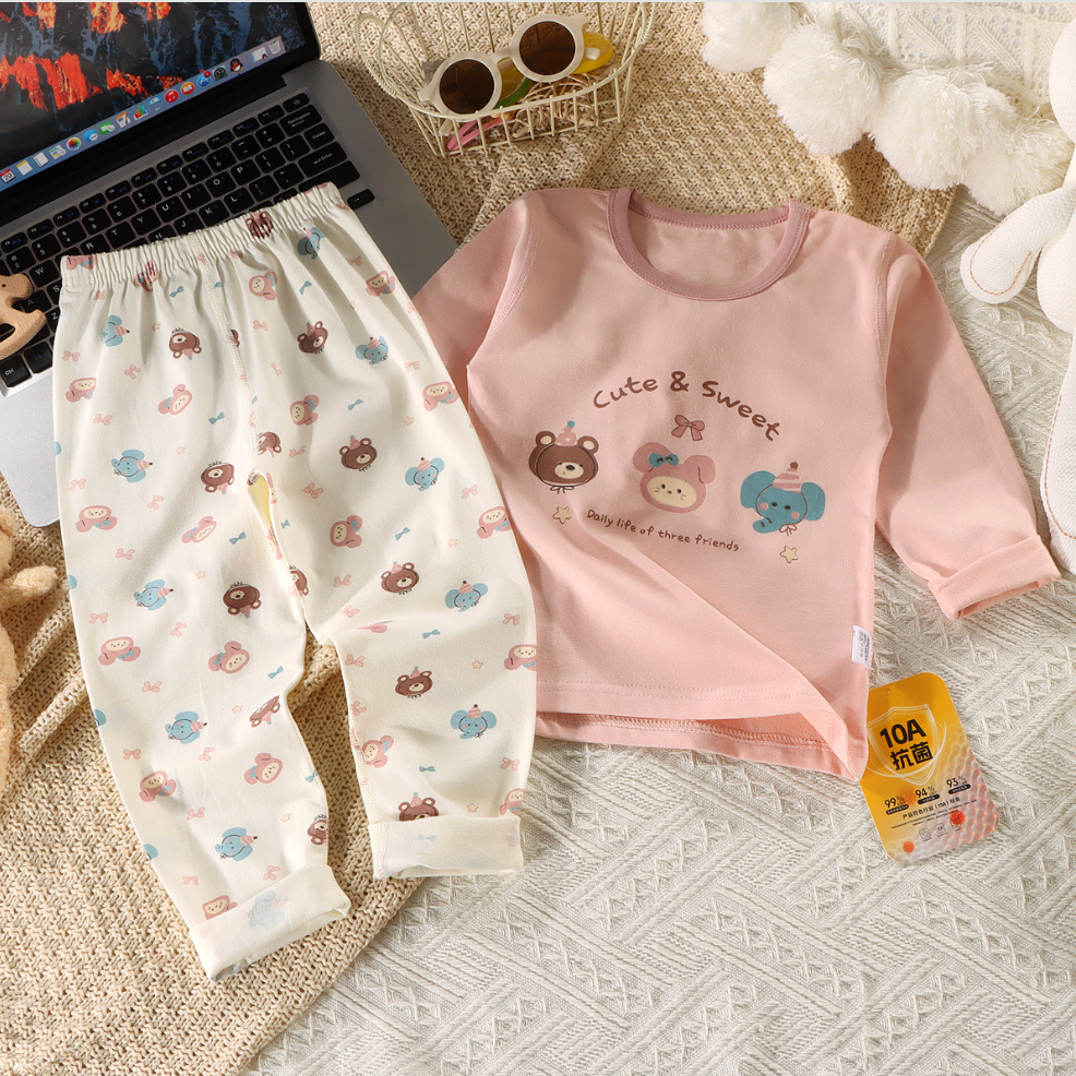 Children's pink shirt and white pants with bear designs on a textured surface.