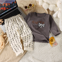 Children's outfit with pants and shirt on a textured surface next to a laptop.