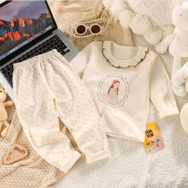 Children's outfit with a white sweater and pants on a textured surface with a laptop and toys.