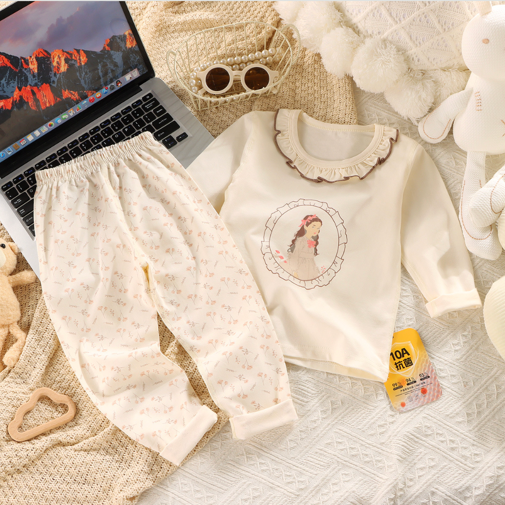Children's outfit with a white sweater and pants on a textured surface with a laptop and toys.