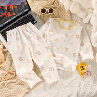 Baby outfit with long-sleeve shirt and pants on a textured surface with a laptop and sunglasses.