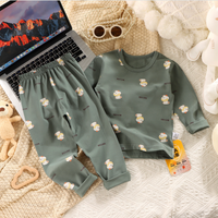 Children's green pajama set with bear pattern on a textured surface with a laptop and toys.