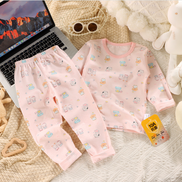 Children's pink pajama set with cartoon patterns on a textured surface next to a laptop.