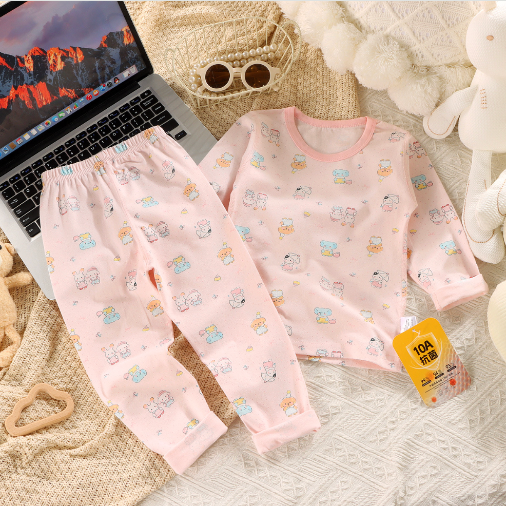 Children's pink pajama set with cartoon patterns on a textured surface next to a laptop.